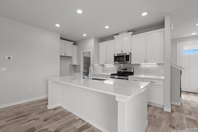 kitchen featuring a kitchen island with sink, light wood-type flooring, sink, white cabinets, and appliances with stainless steel finishes