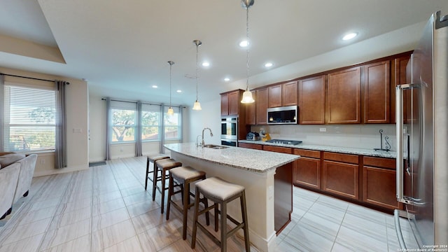 kitchen featuring pendant lighting, a kitchen island with sink, appliances with stainless steel finishes, a breakfast bar, and light stone countertops