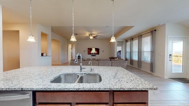 kitchen with ceiling fan, pendant lighting, a center island with sink, sink, and light stone countertops