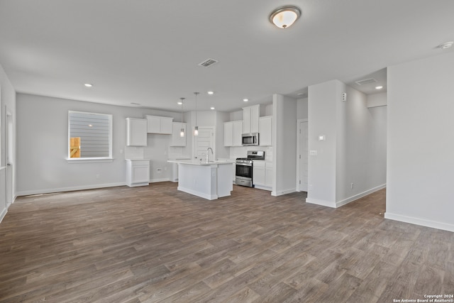 kitchen featuring white cabinets, pendant lighting, a center island with sink, appliances with stainless steel finishes, and hardwood / wood-style floors