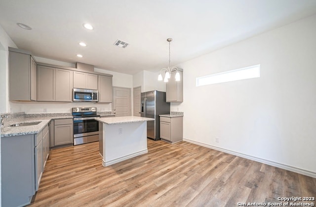 kitchen featuring light hardwood / wood-style floors, gray cabinetry, decorative light fixtures, stainless steel appliances, and a center island