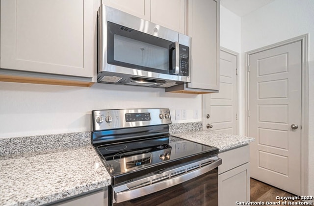 kitchen with stainless steel appliances, dark wood-type flooring, and light stone counters