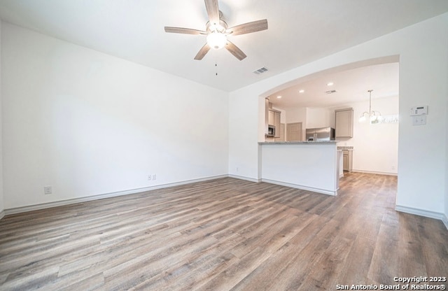 unfurnished living room with wood-type flooring and ceiling fan with notable chandelier