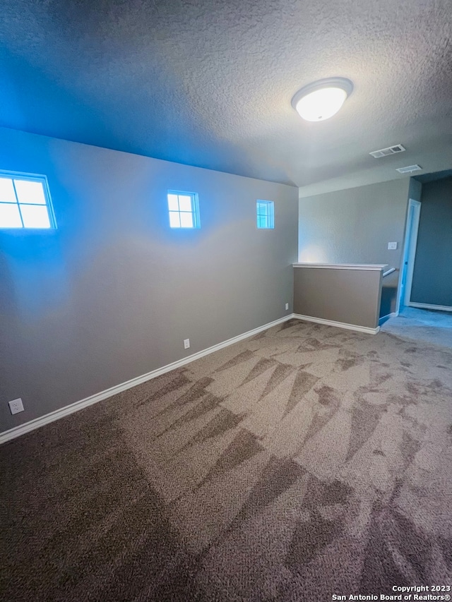 basement featuring a textured ceiling, carpet floors, and a healthy amount of sunlight