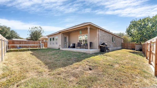 rear view of house with a trampoline, a patio, and a yard