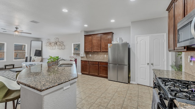 kitchen with ceiling fan, a kitchen island with sink, stainless steel appliances, sink, and backsplash