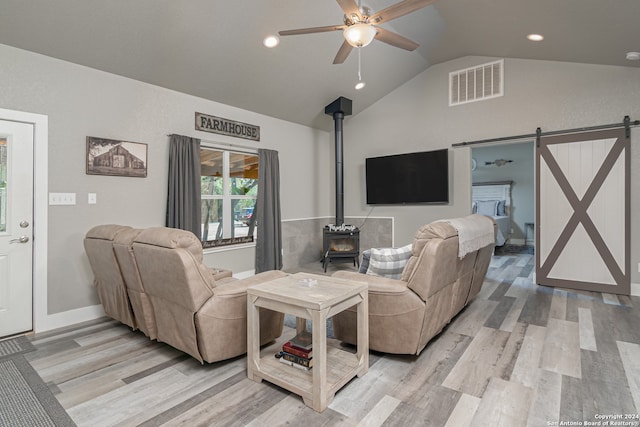 living room with lofted ceiling, light hardwood / wood-style floors, a barn door, and ceiling fan