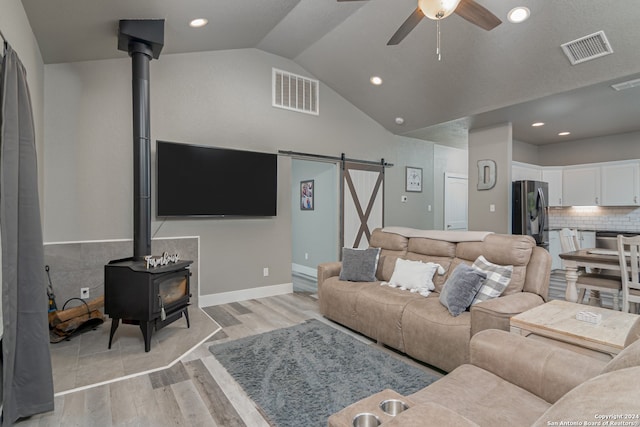 living room featuring a barn door, light wood-type flooring, ceiling fan, a wood stove, and lofted ceiling