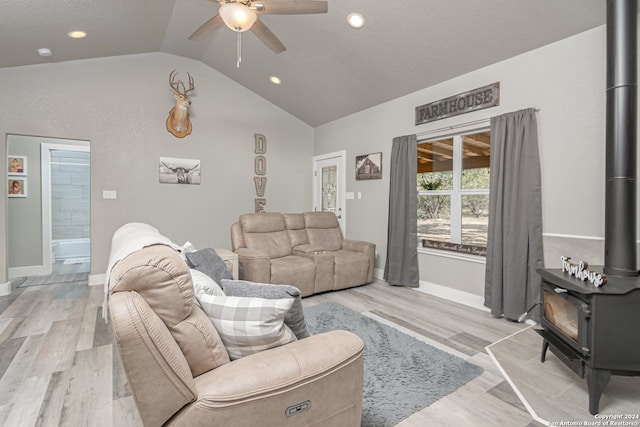 living room with lofted ceiling, ceiling fan, light hardwood / wood-style floors, and a wood stove