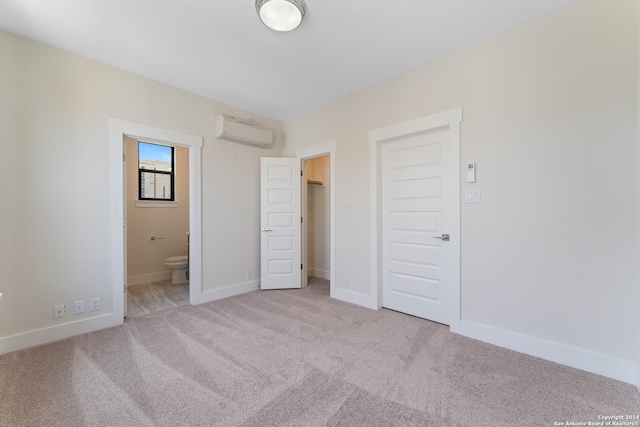 unfurnished bedroom featuring ensuite bath, a wall mounted air conditioner, a closet, and light colored carpet