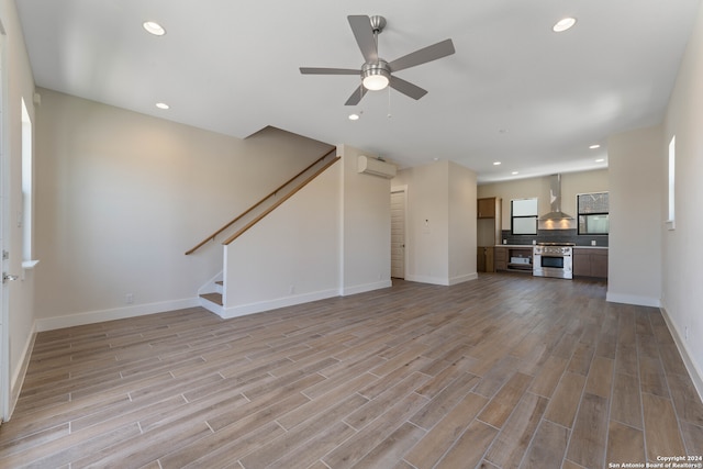 unfurnished living room featuring a wall unit AC, light hardwood / wood-style flooring, and ceiling fan