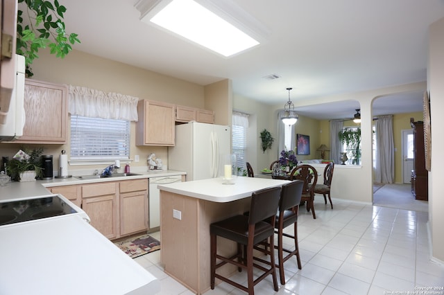 kitchen with light brown cabinetry, a kitchen island, and white appliances