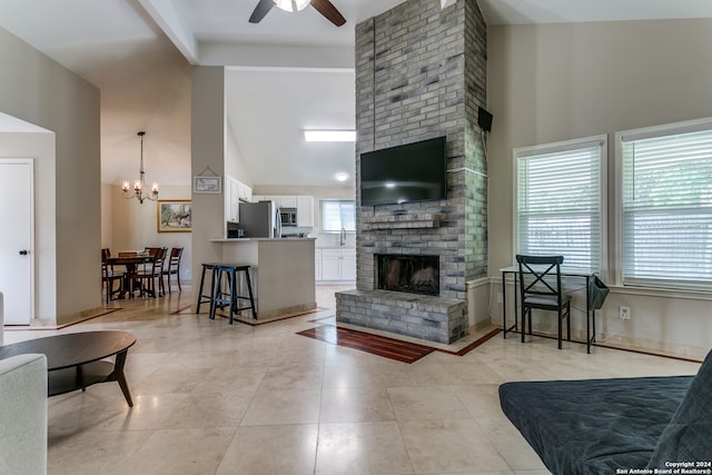 living room featuring a fireplace, ceiling fan with notable chandelier, a high ceiling, and a healthy amount of sunlight