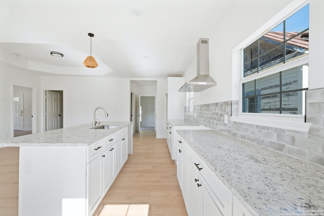 kitchen featuring sink, hanging light fixtures, wall chimney range hood, and a center island with sink