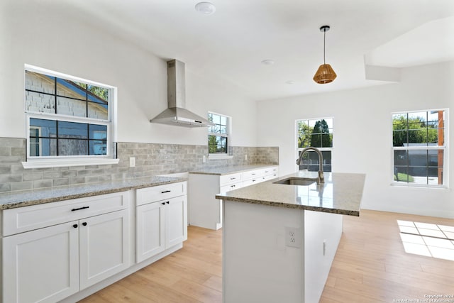 kitchen with a kitchen island with sink, white cabinets, hanging light fixtures, sink, and range hood