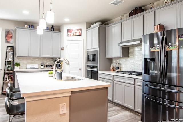 kitchen featuring light wood-type flooring, decorative backsplash, a kitchen island with sink, stainless steel appliances, and sink