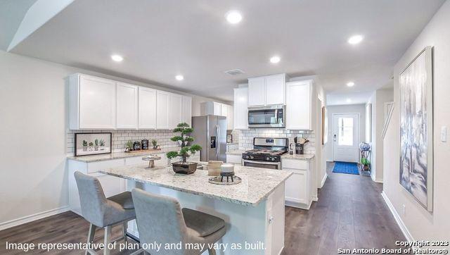 kitchen with white cabinets, dark wood-style floors, stainless steel appliances, backsplash, and a kitchen island