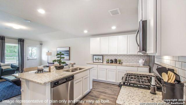 kitchen with stainless steel dishwasher, a sink, white cabinets, backsplash, and visible vents