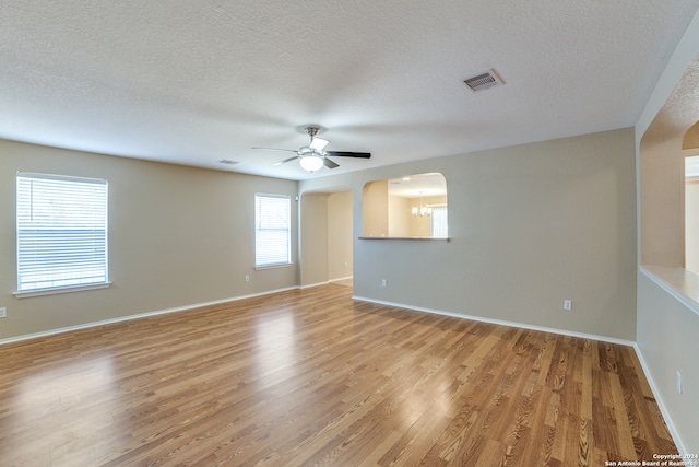 spare room featuring ceiling fan with notable chandelier, light hardwood / wood-style floors, and a textured ceiling