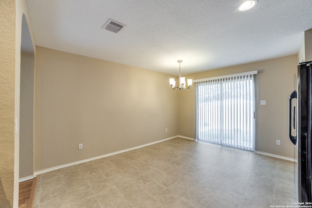 spare room featuring a notable chandelier and a textured ceiling