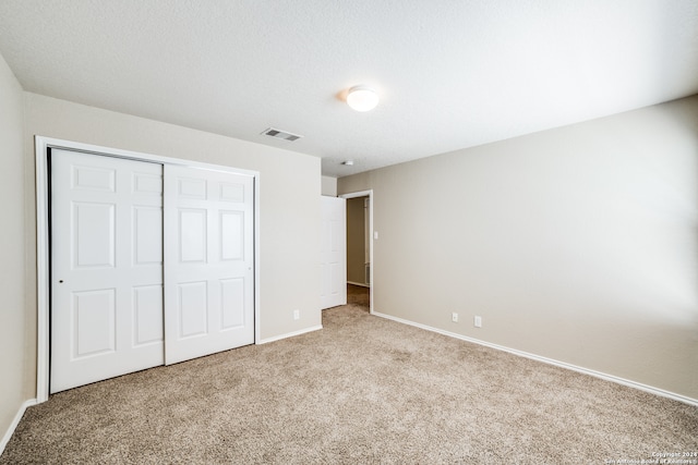 unfurnished bedroom featuring a closet, a textured ceiling, and light carpet