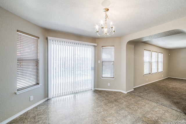 carpeted empty room featuring an inviting chandelier and a textured ceiling