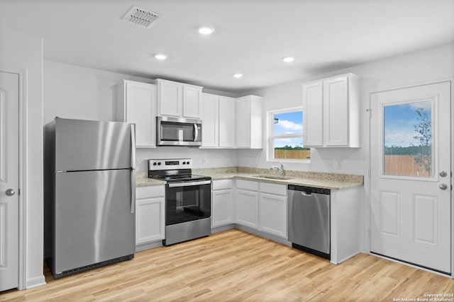 kitchen with appliances with stainless steel finishes, white cabinetry, sink, and light hardwood / wood-style flooring