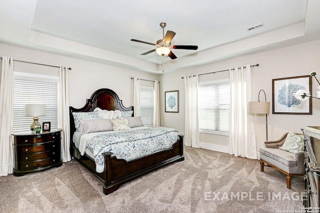 carpeted bedroom featuring visible vents, baseboards, a ceiling fan, and a tray ceiling