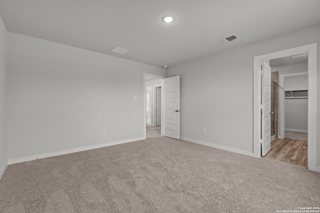 unfurnished bedroom with a walk in closet, light carpet, and a closet