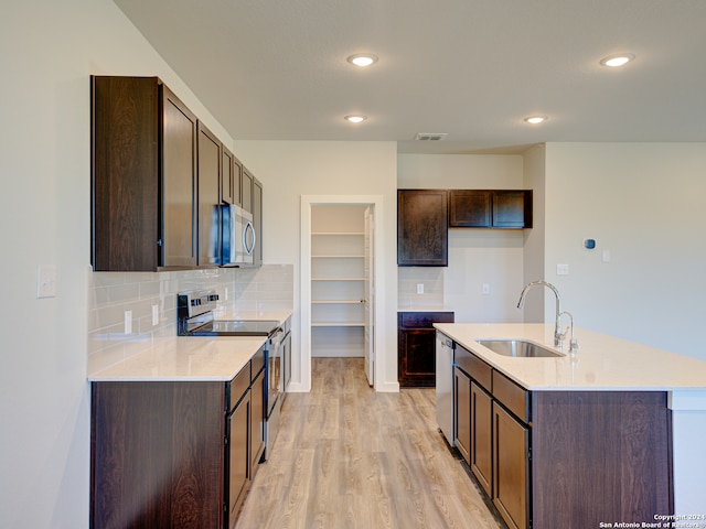 kitchen featuring decorative backsplash, appliances with stainless steel finishes, a kitchen island with sink, sink, and light hardwood / wood-style flooring