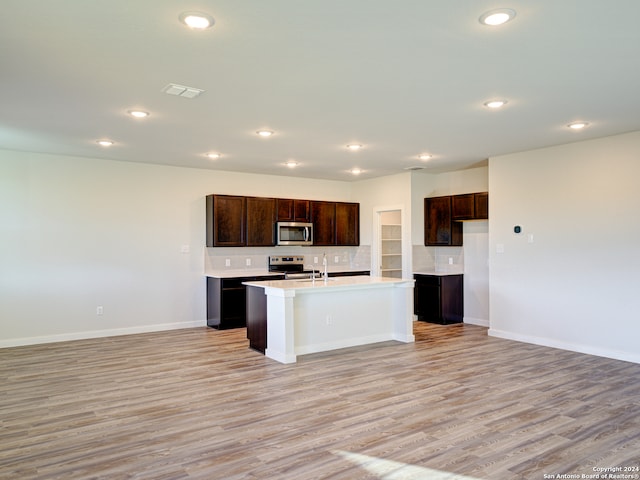 kitchen with a center island with sink, backsplash, appliances with stainless steel finishes, and light hardwood / wood-style flooring