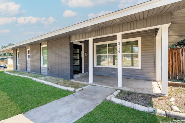 view of exterior entry featuring a yard and covered porch