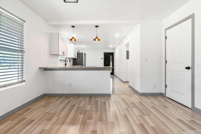 kitchen with white cabinets, kitchen peninsula, decorative light fixtures, stainless steel refrigerator, and light wood-type flooring