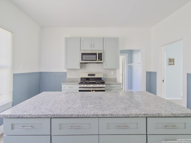 kitchen with light stone countertops, stainless steel appliances, plenty of natural light, and gray cabinetry