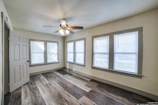 empty room with a textured ceiling, wood finished floors, ceiling fan, and baseboards