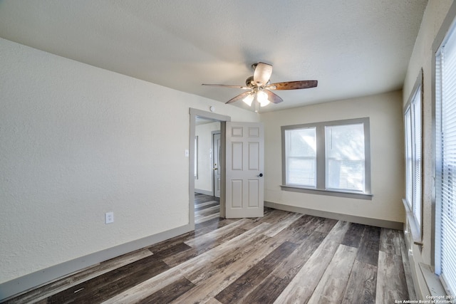 empty room with wood finished floors, a textured wall, baseboards, and a ceiling fan