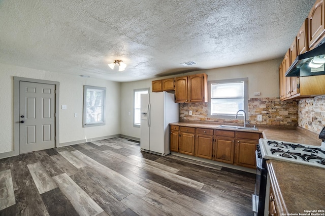kitchen with tasteful backsplash, gas stove, white refrigerator with ice dispenser, brown cabinets, and a sink