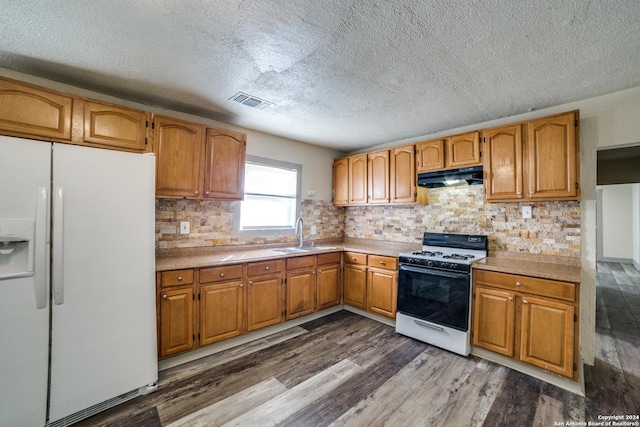 kitchen featuring white appliances, a textured ceiling, under cabinet range hood, dark wood finished floors, and a sink