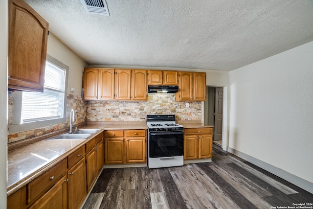 kitchen with dark wood-style flooring, white range with gas cooktop, under cabinet range hood, visible vents, and a sink