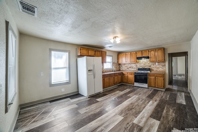 kitchen featuring visible vents, white fridge with ice dispenser, under cabinet range hood, gas stove, and dark wood-type flooring