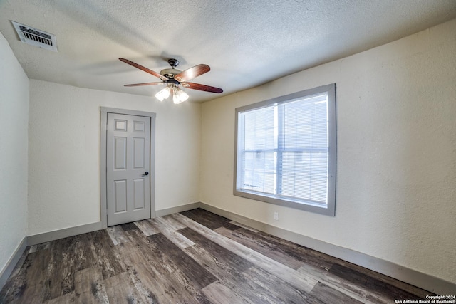 unfurnished room with ceiling fan, a textured ceiling, visible vents, wood finished floors, and baseboards