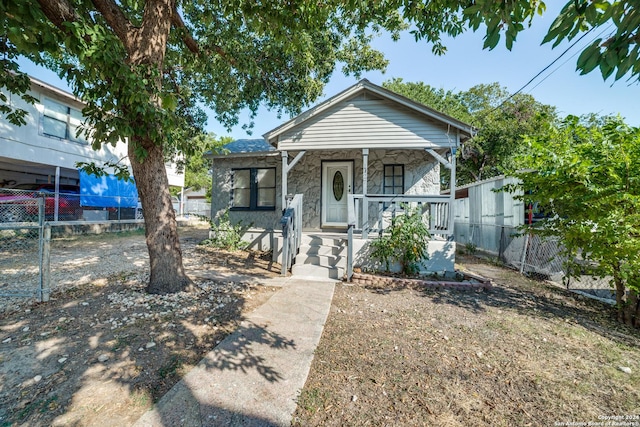 shotgun-style home with a porch, fence, and stone siding
