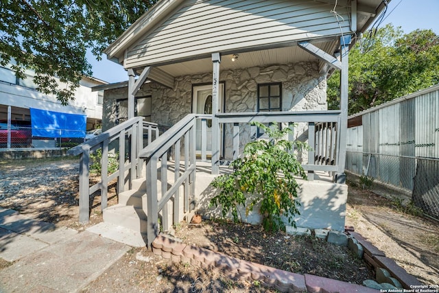 exterior space featuring a porch, fence, and stone siding
