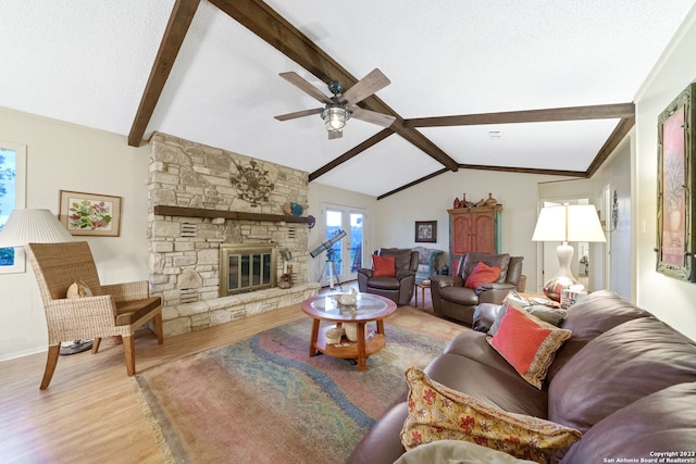 living room featuring a stone fireplace, vaulted ceiling with beams, light hardwood / wood-style floors, and ceiling fan