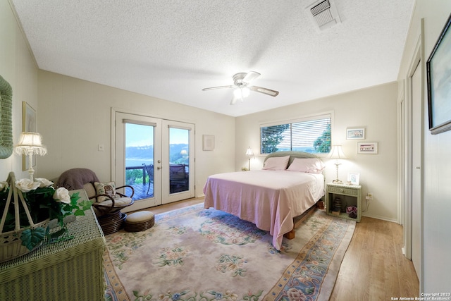 bedroom featuring light wood-type flooring, ceiling fan, french doors, access to exterior, and a textured ceiling