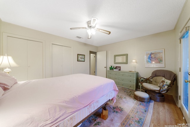 bedroom featuring a textured ceiling, two closets, light wood-type flooring, and ceiling fan