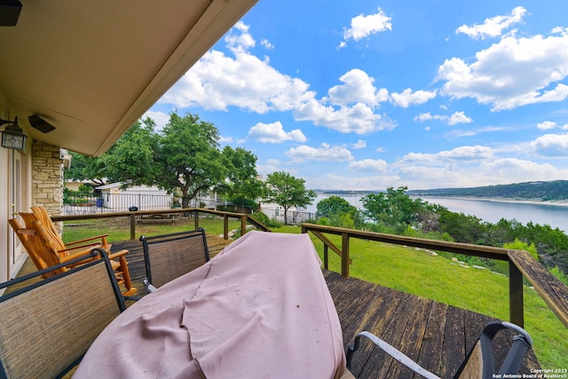 wooden terrace featuring a water view and a lawn