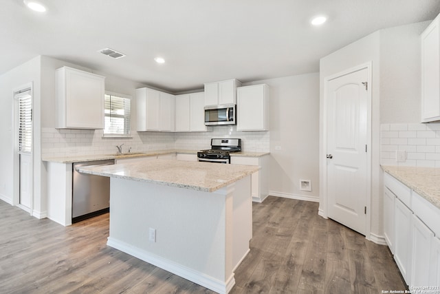 kitchen featuring light stone counters, white cabinets, a kitchen island, appliances with stainless steel finishes, and light wood-type flooring