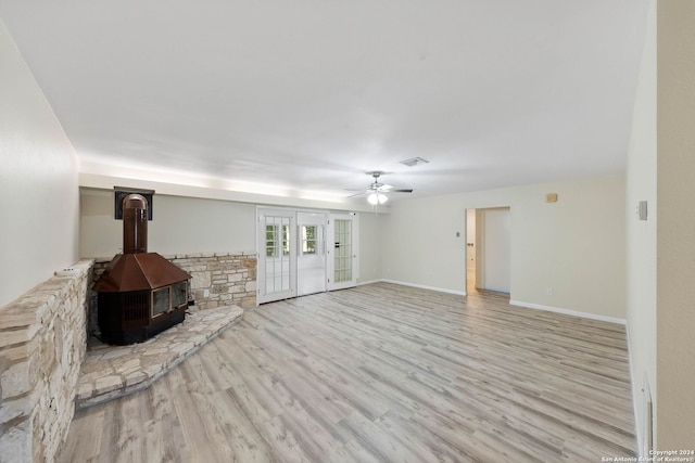 unfurnished living room with a wood stove, ceiling fan, and light hardwood / wood-style flooring