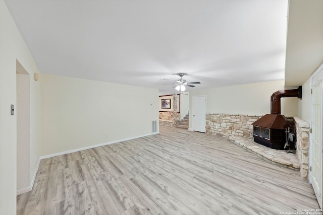 unfurnished living room featuring ceiling fan, light hardwood / wood-style floors, and a wood stove